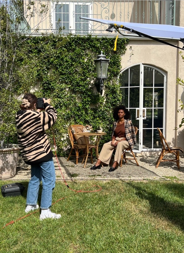 A photographer captures an image of a model sitting at an outdoor table wearing a fall outfit and the LifeStride Sonoma loafer.