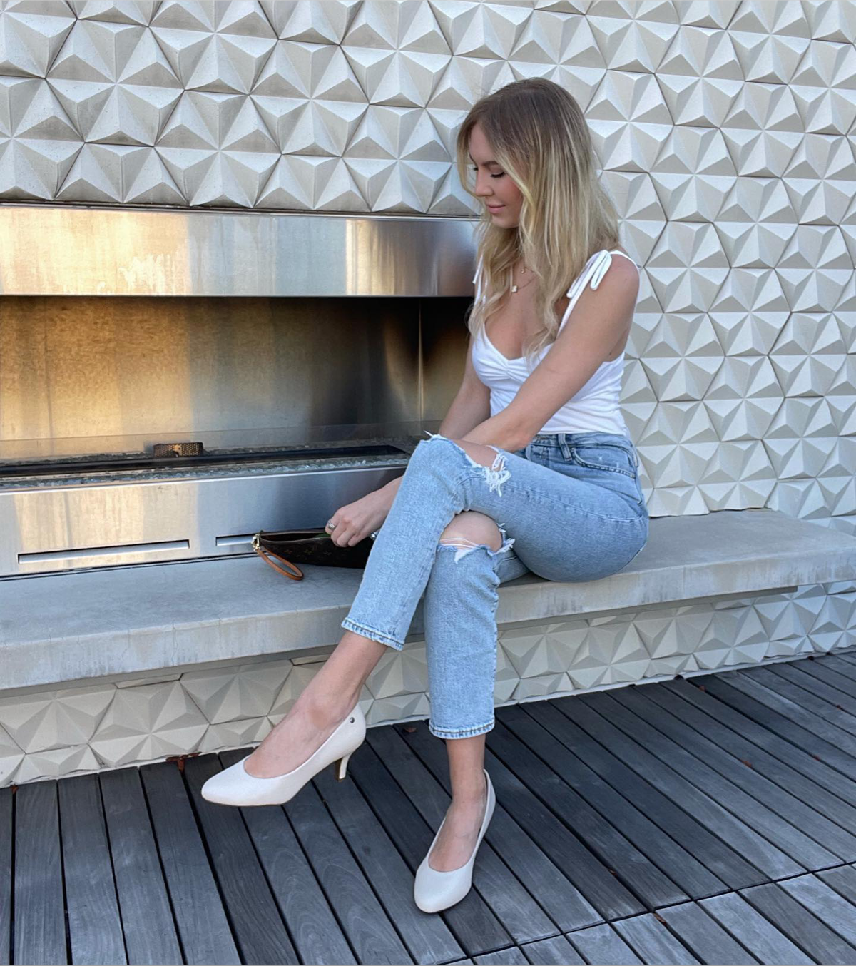 Influencer @_alexaschmitz styles the LifeStride Parigi pump in almond milk with ripped skinny jeans and a dressy white tank top next to an outdoor fireplace.