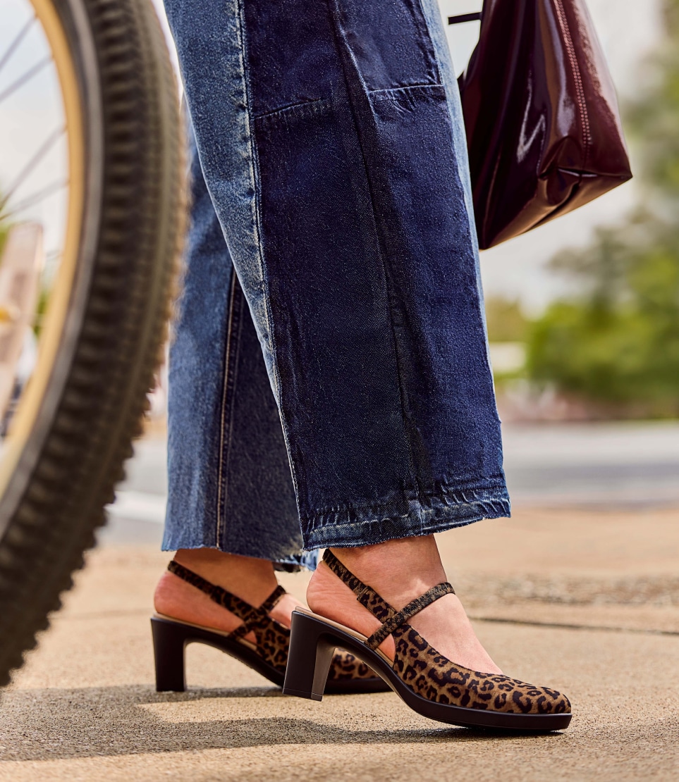 a model wearing leopard print LifeStride heels while carrying a purse next to a bicycle wheel