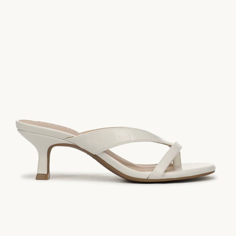 A side view of a white heeled sandal with the toe facing to the right. 