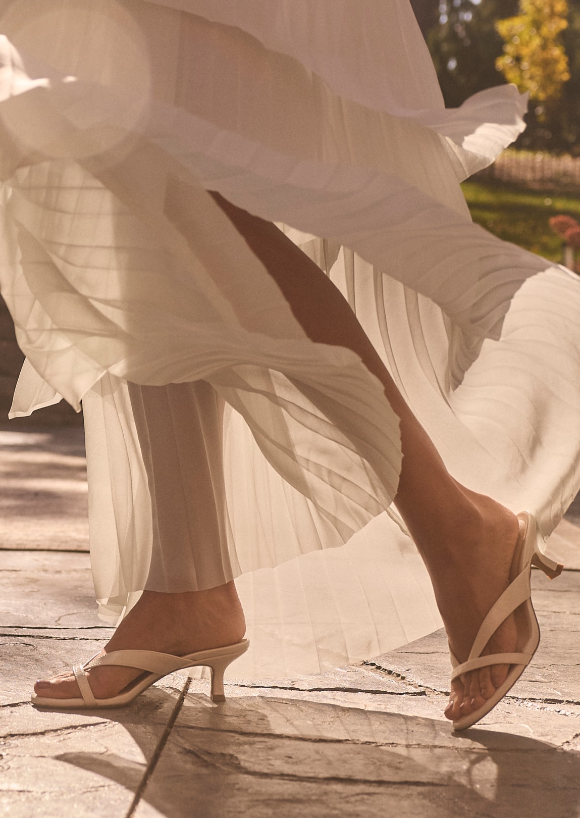 A woman wearing a flowy white dress with cream-colored heeled sandals. 