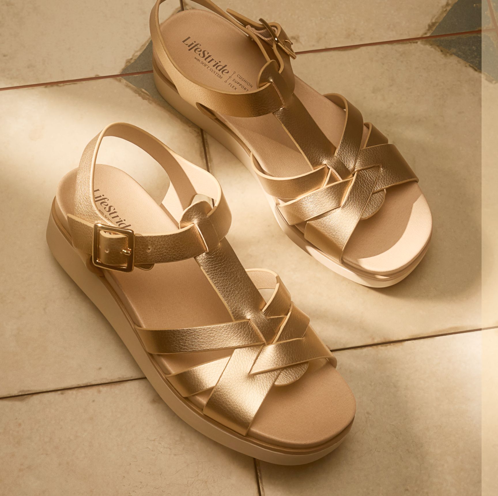 A top view of a pair of women's strappy wedge sandals in gold faux leather displayed on a tile floor.