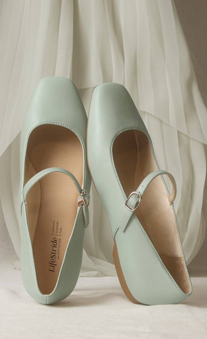 A pair of jade green Mary Jane flats displayed vertically on a white fabric backdrop. 