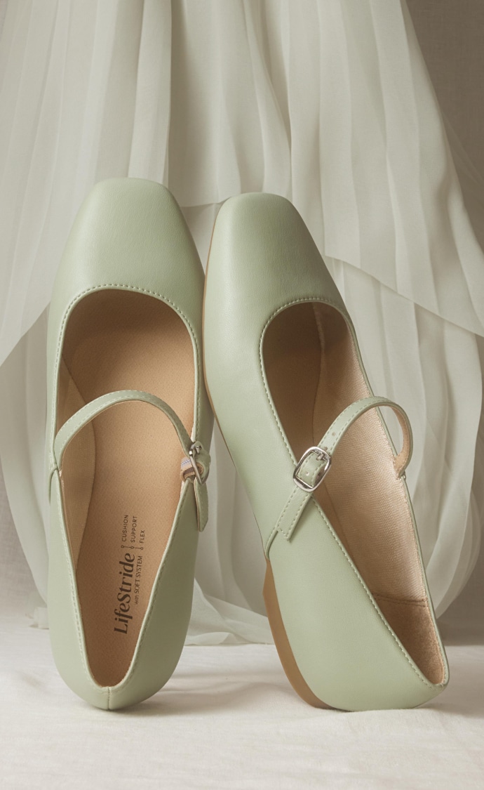 A pair of jade green Mary Jane flats displayed vertically on a white fabric backdrop. 