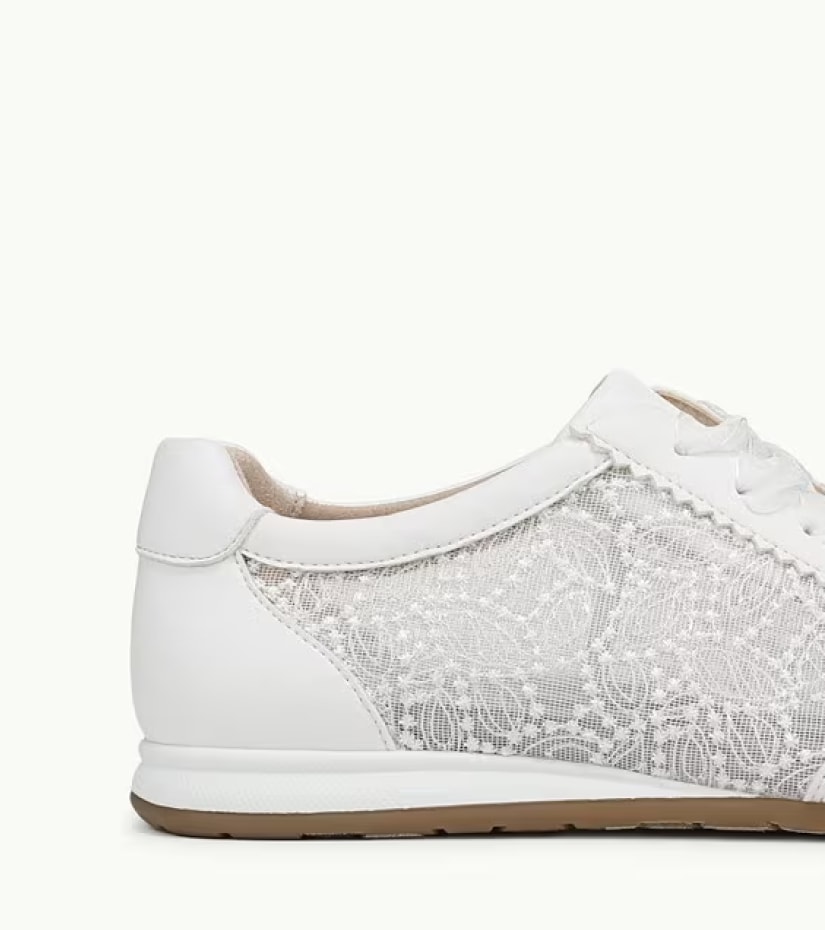 A partial side view of a white sneaker with a mesh side panel. 