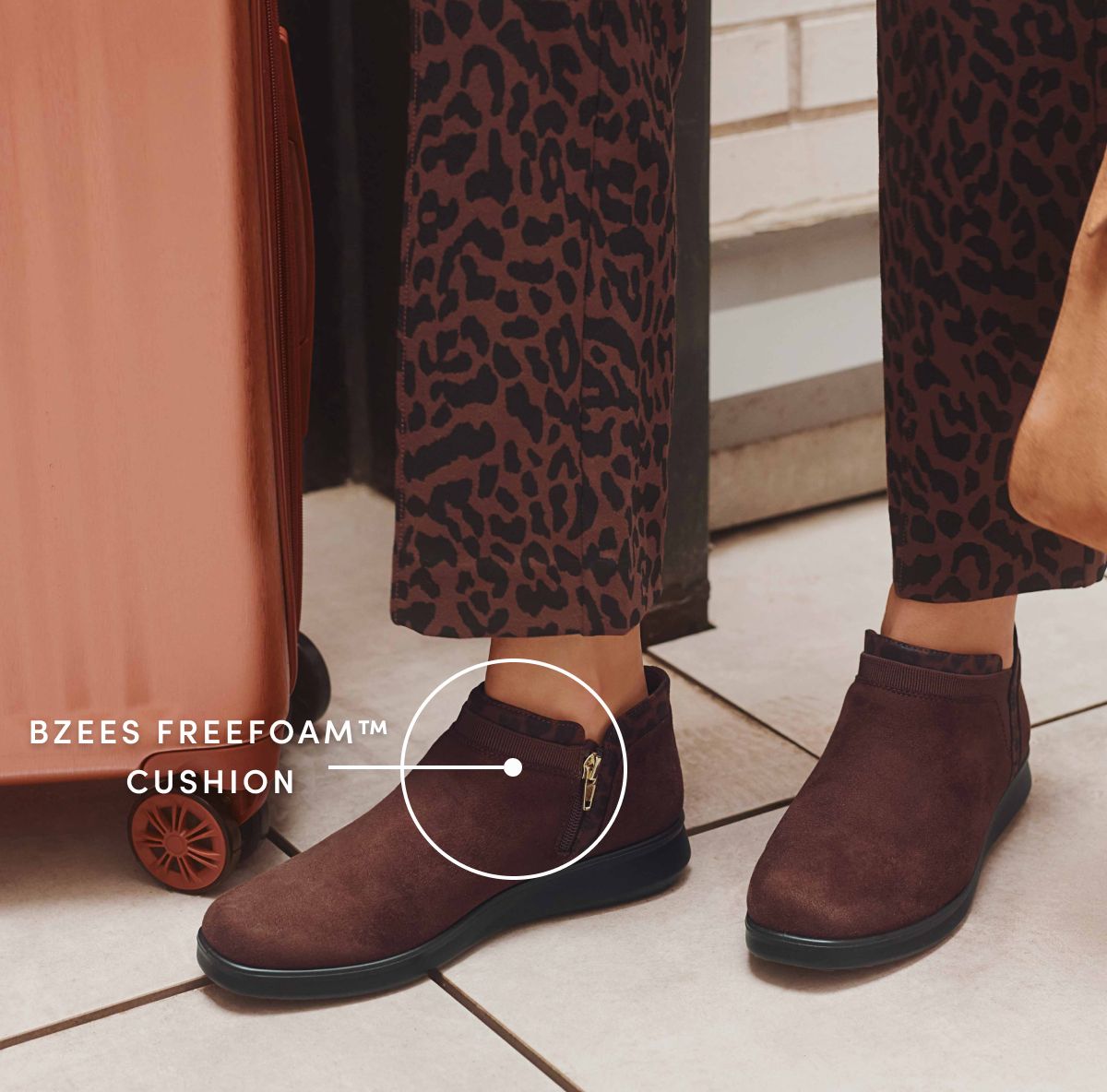 Woman standing next to luggage wearing leopard print pants and brown ankle boots. White text reads 